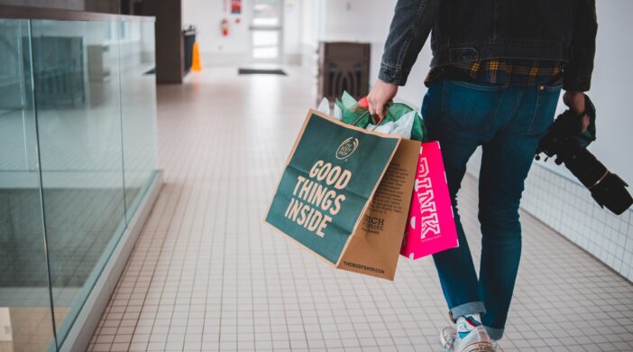 person walking while carrying a camera and paper bags